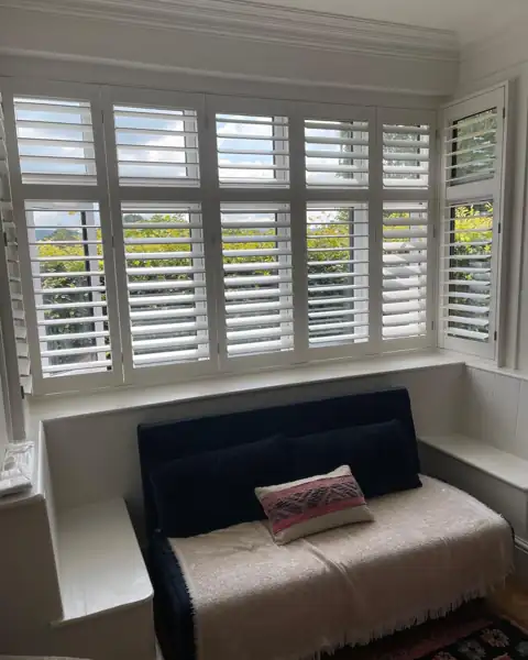 Full height hardwood shutters across a bay window