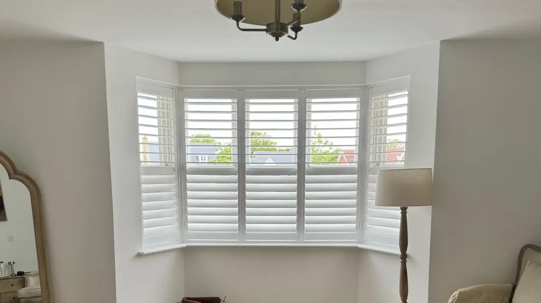 Hardwood shutters fitted across a bay window in an Essex bedroom